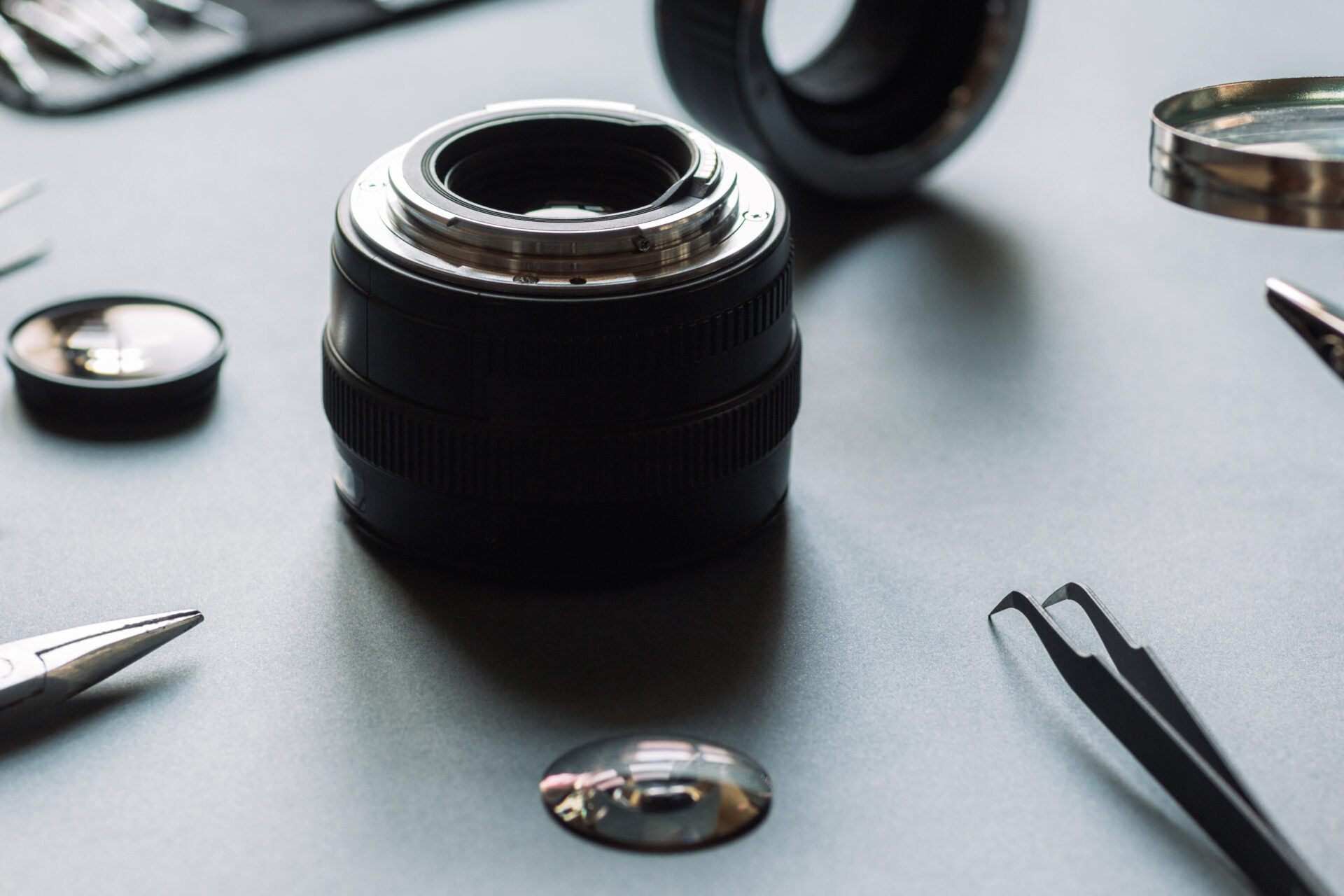 Disassembled lens with optical lenses and tools on a workbench.